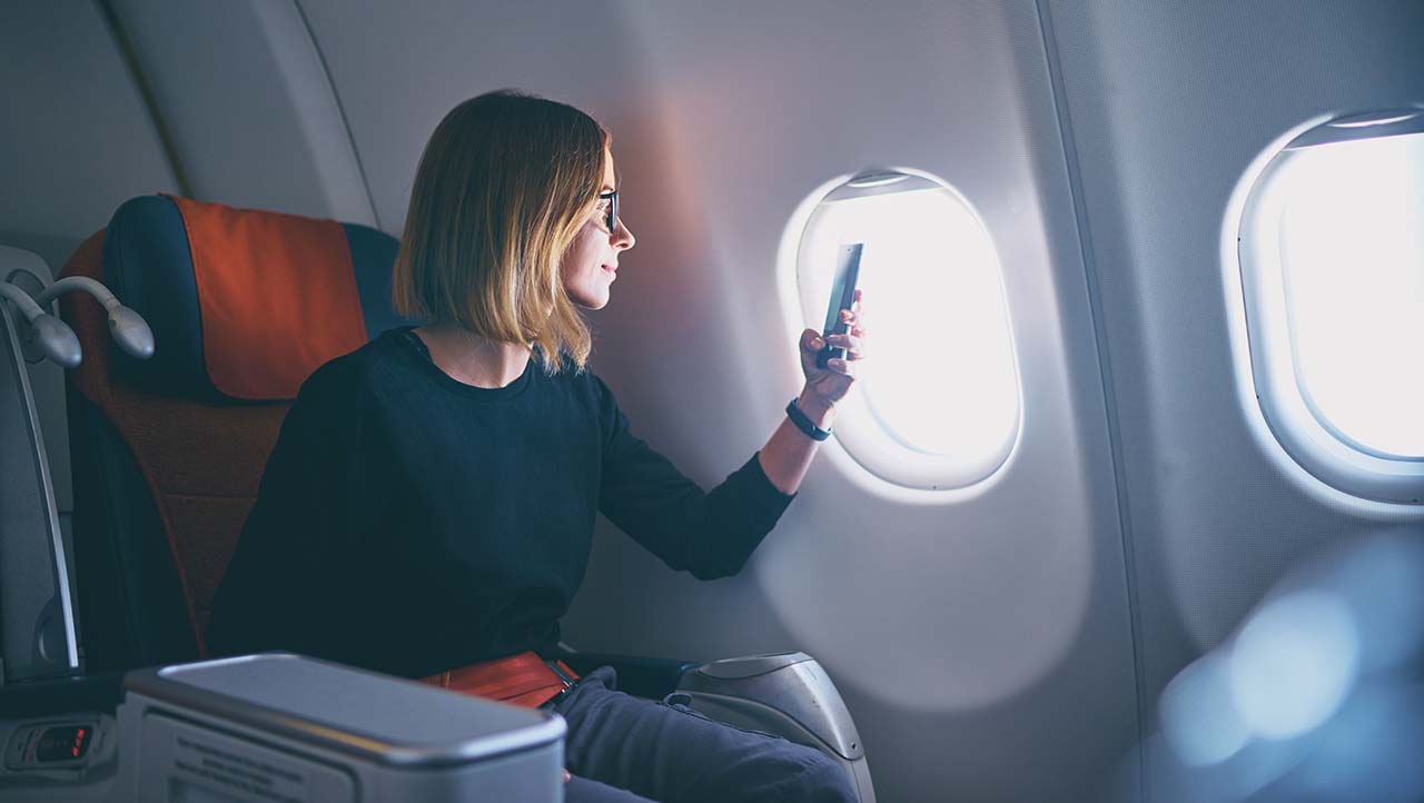 Business woman taking photo on smartphone while sitting in airplane Medium Business woman taking photo on smartphone while sitting in airplane