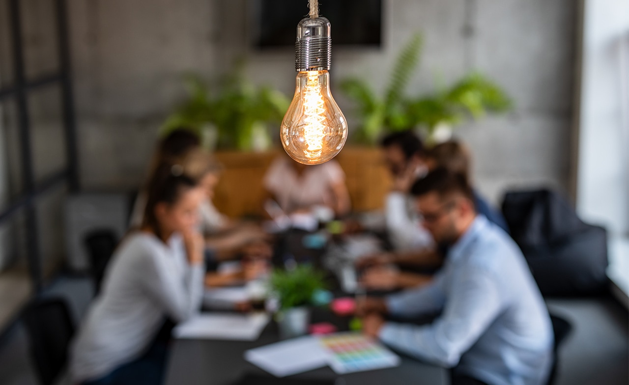 Young creative business people meeting in an office with a lightbulb in the foreground shining overhead