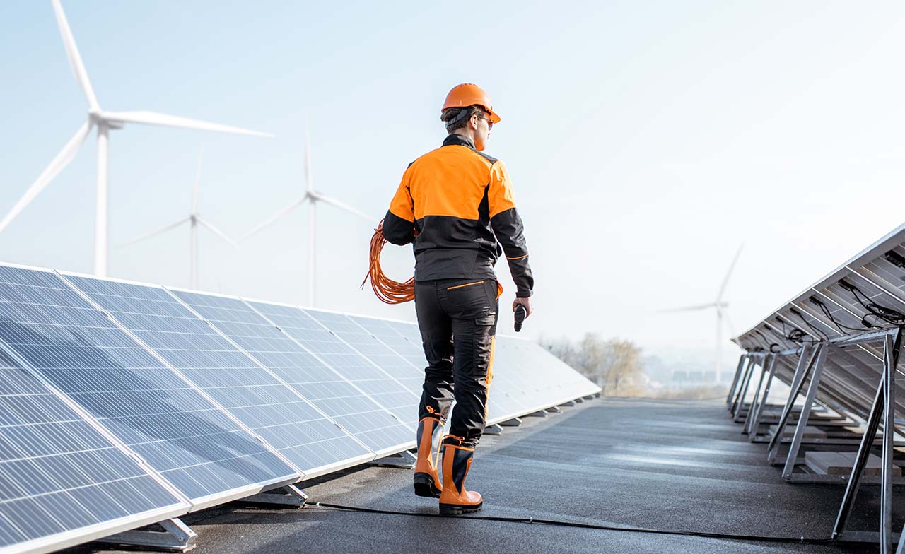 Person walking along solar panels with windmills in the distance Person walking along solar panels with windmills in the distance