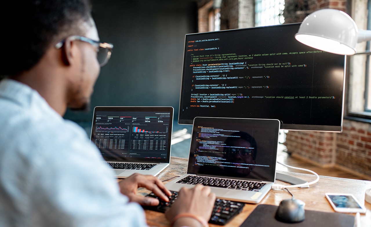 Male programmer coding with three monitors