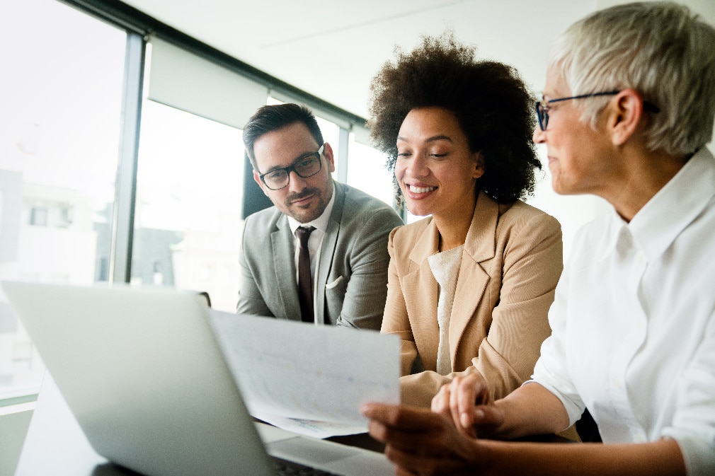 Three professionals reviewing data on a document and laptop