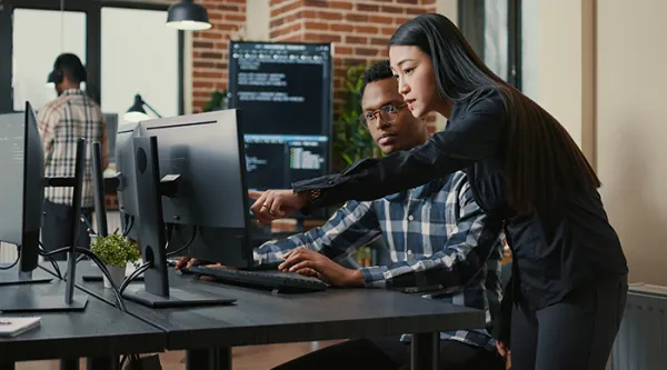 Two programers holding laptop with coding interface walking towards desk and sitting down…