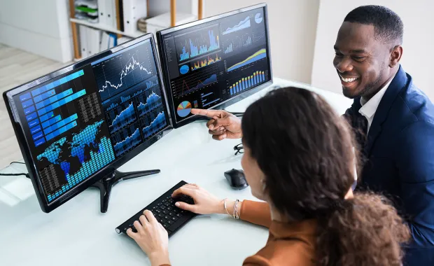 two consultants analyze data on two monitors