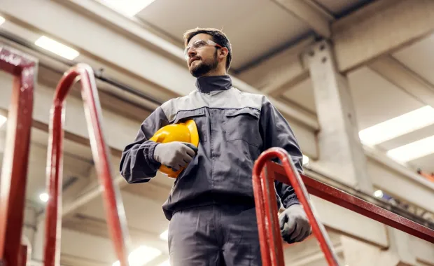 Male industrial factory worker with safety glasses holding hard hat