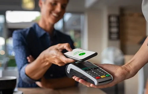 Person betaler med mobiltelefon via kontaktløs betalingsterminal i butikk