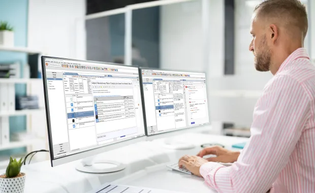 Junger Mann sitzt an seinem Arbeitsplatz und schaut in zwei Bildschirme