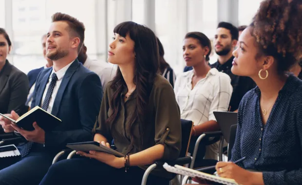 Training session with audience of professionals sitting in chairs holding notebooks
